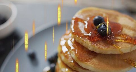 Pouring maple syrup over stack of golden pancakes with blueberries, close-up drizzle