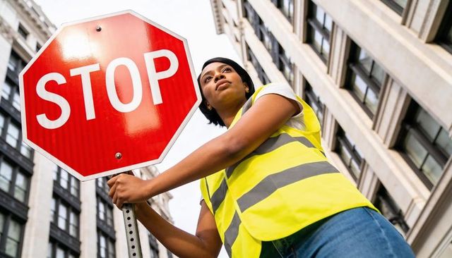 Holding stop sign on urban street by worker wearing high-visibility reflective vest