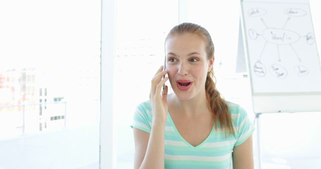 Excited young woman talking on phone in bright office environment - Download Free Stock Images Pikwizard.com