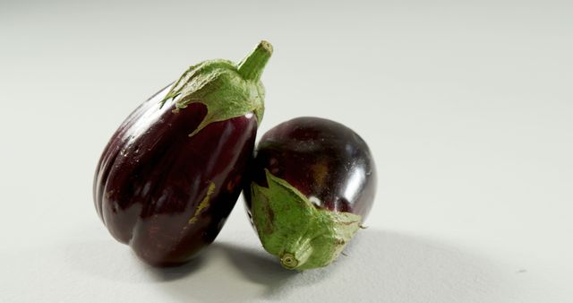 Two fresh eggplants resting against each other, isolated against a white background. Perfect for use in articles, blogs, and websites promoting healthy eating, vegetarian recipes, organic produce, and agriculture. Ideal for educational content about vegetables, nutrition tips, or cooking websites.