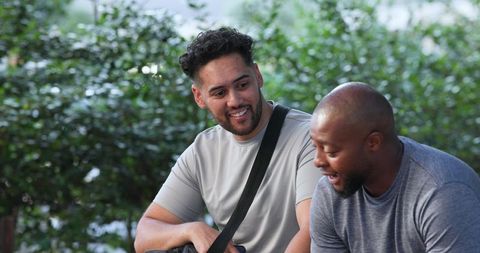 Two men sitting on park bench smiling and chatting, casual friendship relaxation
