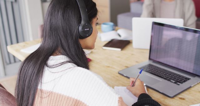 Woman Wearing Headphones Working on Laptop and Taking Notes - Download Free Stock Images Pikwizard.com