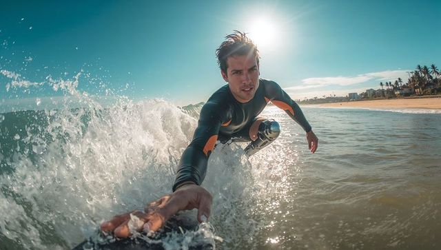 Male surfer carving close-up on sunny beach showing metallic prosthetic leg and ocean spray