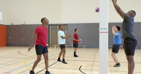 Diverse young men practicing indoor volleyball spiking, blocking, team training drills