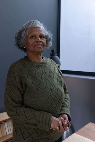 Senior woman in cozy sweater standing by study desk