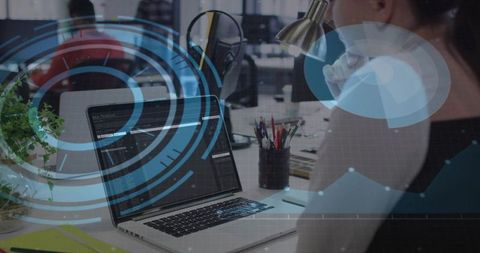 Developer coding on laptop in open-plan office with futuristic data visualization overlays