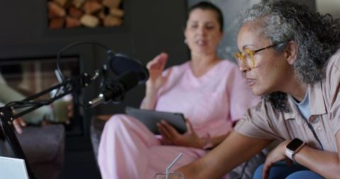 Collaborative podcast recording session with women leaning, reaching, using boom mic