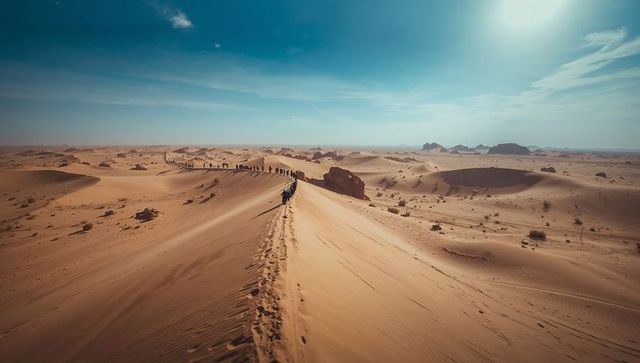Group walking along desert dune ridge leaving footprints on sunlit sand during long trek