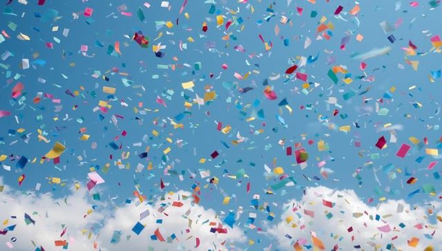 Colorful Confetti Falling against Blue Sky with White Clouds