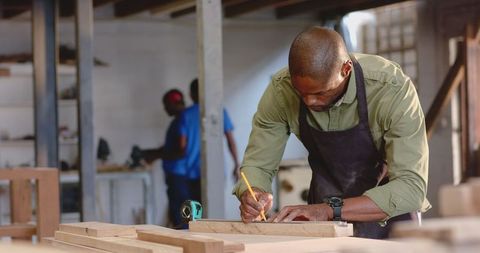 Artisan measuring wood plank in industrial workshop
