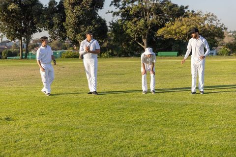 Sunlit cricket teammates standing on green field in white uniforms during golden hour