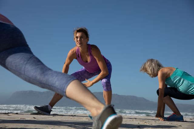 Group of Caucasian female friends enjoying exercising on a beach on a sunny day, practicing yoga and stretching with sea in the background.
