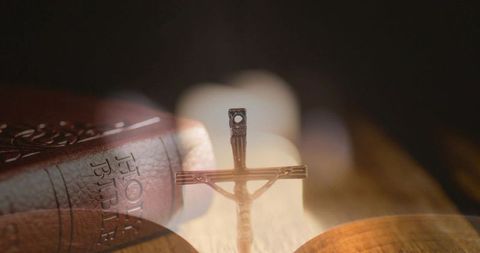 Metal crucifix standing on altar with holy bible and warm candlelight bokeh, reverent devotional