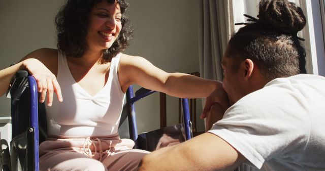 Woman using wheelchair engaging with her male companion, sharing a moment of joy in a well-lit room. Suitable for themes of companionship, support, inclusive relationships, mental health, and disability awareness. Can be used in promotional materials, social media posts, or articles about friendship and support systems.