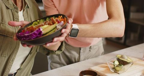 Diverse couple sharing avocado poke bowl at kitchen counter, healthy plant-based meal prep