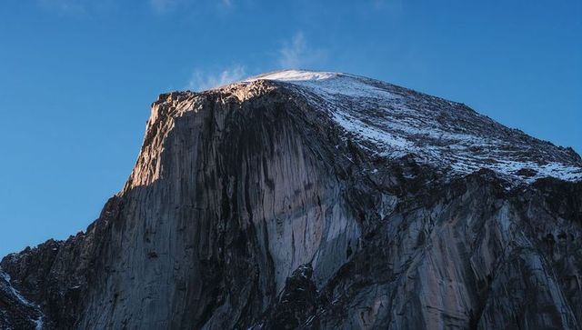Sunlit Granite Dome with Snow-Capped Crest and Vertical Rock Faces at Blue Sky Dawn