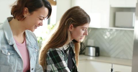 Sunlit friends washing dishes together in modern kitchen sharing household chores