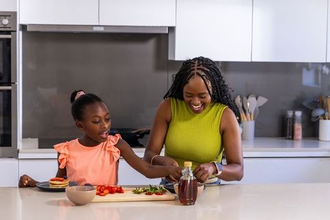 African mother and daughter making pancakes together in bright modern kitchen