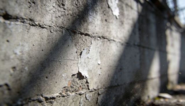 Sunlit weathered concrete wall showing peeling paint, cracked seams, dust and diagonal shadows