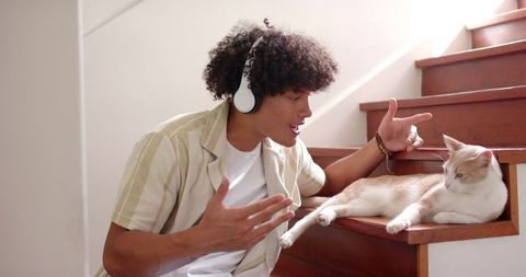 Man Wearing Headphones Interacting with Cat on Wooden Stairs