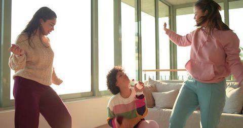 Diverse friends dancing and singing karaoke in bright sunlit apartment living room