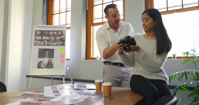 Professional Photographer Sharing Camera Techniques with Assistant in Modern Office - Download Free Stock Images Pikwizard.com