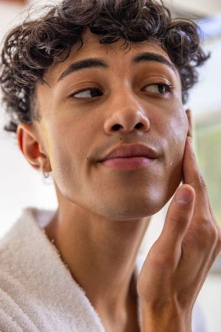 Young Man Engaging in Morning Skincare Routine by Window Light