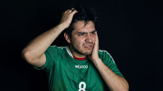 Hispanic soccer player wearing mexico jersey holding head showing agony and frustration