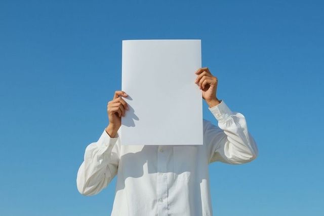 Man in white shirt holding blank poster against blue sky