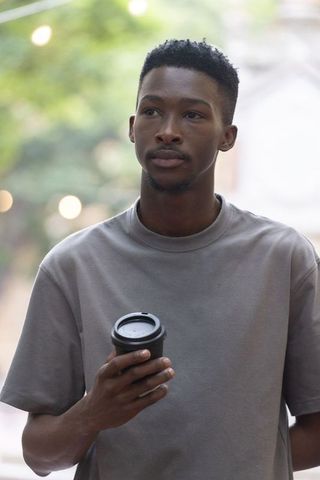 African man holding takeaway cup standing in courtyard looking contemplative and calm