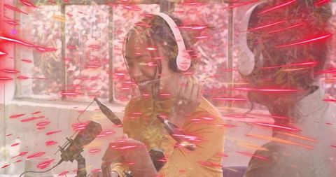 Smiling woman adjusting white headphones, cohost recording at mic with pink light streaks