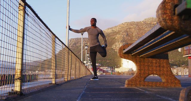 Focused african american man stretching, exercising outdoors by seaside. fitness, healthy and active lifestyle concept.