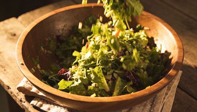 Rustic wooden bowl tossing fresh mixed greens with herb dressing in warm golden light