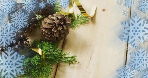 Rustic holiday pinecones and fir sprigs decorating light wood planks with gold ribbon and snowflake 