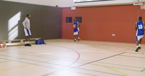 Basketball players practicing and dribbling on indoor hardwood court with coach observing