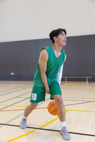 Young asian male dribbling basketball in green jersey no.10 on indoor gym court