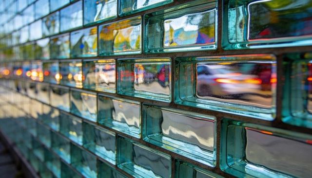 Turquoise glass block facade reflecting urban taillights and twilight traffic motion glow