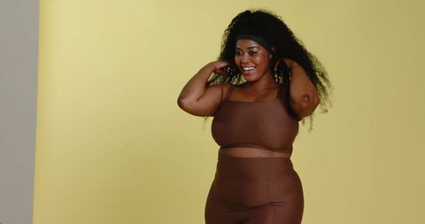 Confident african american woman modeling brown athleisure set smiling on yellow backdrop