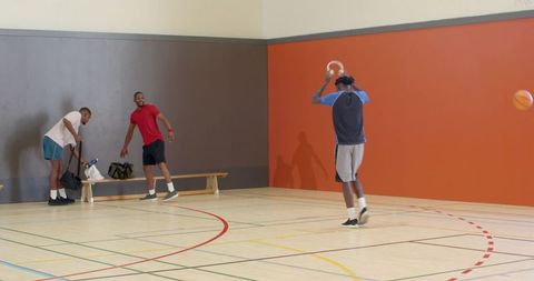 Male basketball players practicing passing drill on indoor court with bench and bags