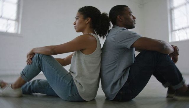 Contemplative couple sitting back-to-back on minimal floor wearing jeans and sneakers