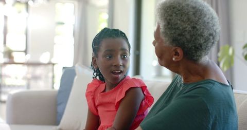 African american grandmother and granddaughter sharing warm conversation on sofa