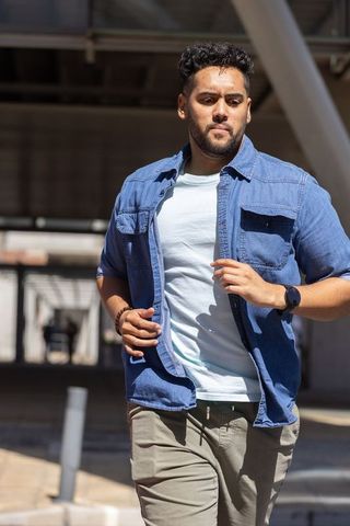 Confident african american man walking through urban walkway in denim shirt and smartwatch
