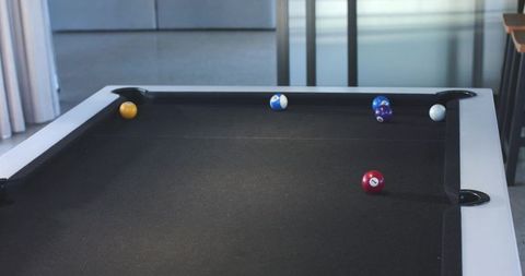 Minimalist lounge with modern black-felt pool table, white rails and scattered billiard balls
