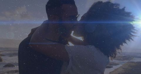 Couple Embracing and Kissing at Sunset on Rocky Shore with Romantic Backlight