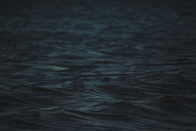 Image capturing dark ocean waves under the soft light of dusk, creating a mystical and serene atmosphere. Ideal for backgrounds, desktop wallpapers, or mood-setting visuals in creative projects involving nature, tranquility, and contemplation.