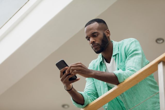 Low angle view of an African-American using a smartphone while standing and arms against a wooden rail