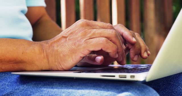 Senior person typing on laptop outdoors. A close-up of elderly hands on keyboard, highlighting technology use by aged individuals. Ideal for tech articles, elder education resources, and healthcare blogs.