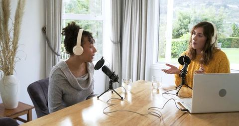 Diverse female co-hosts recording podcast in bright home studio, casual interview talk
