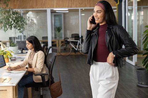 Young professionals talking on smartphone in modern coworking office with colleague working