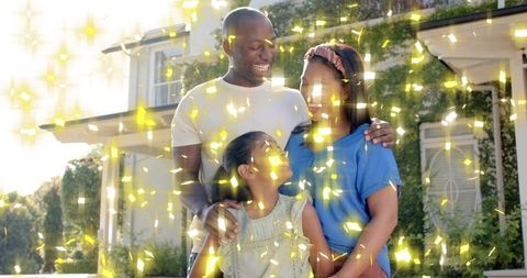 Smiling family hugging outside suburban home with golden confetti and warm sunlight